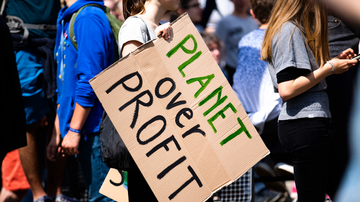 Jovem segura cartaz com os dizeres "Planeta acima de lucro" durante protesto