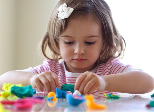 Criança brincando de massinha na mesa (Foto: Shutterstock)