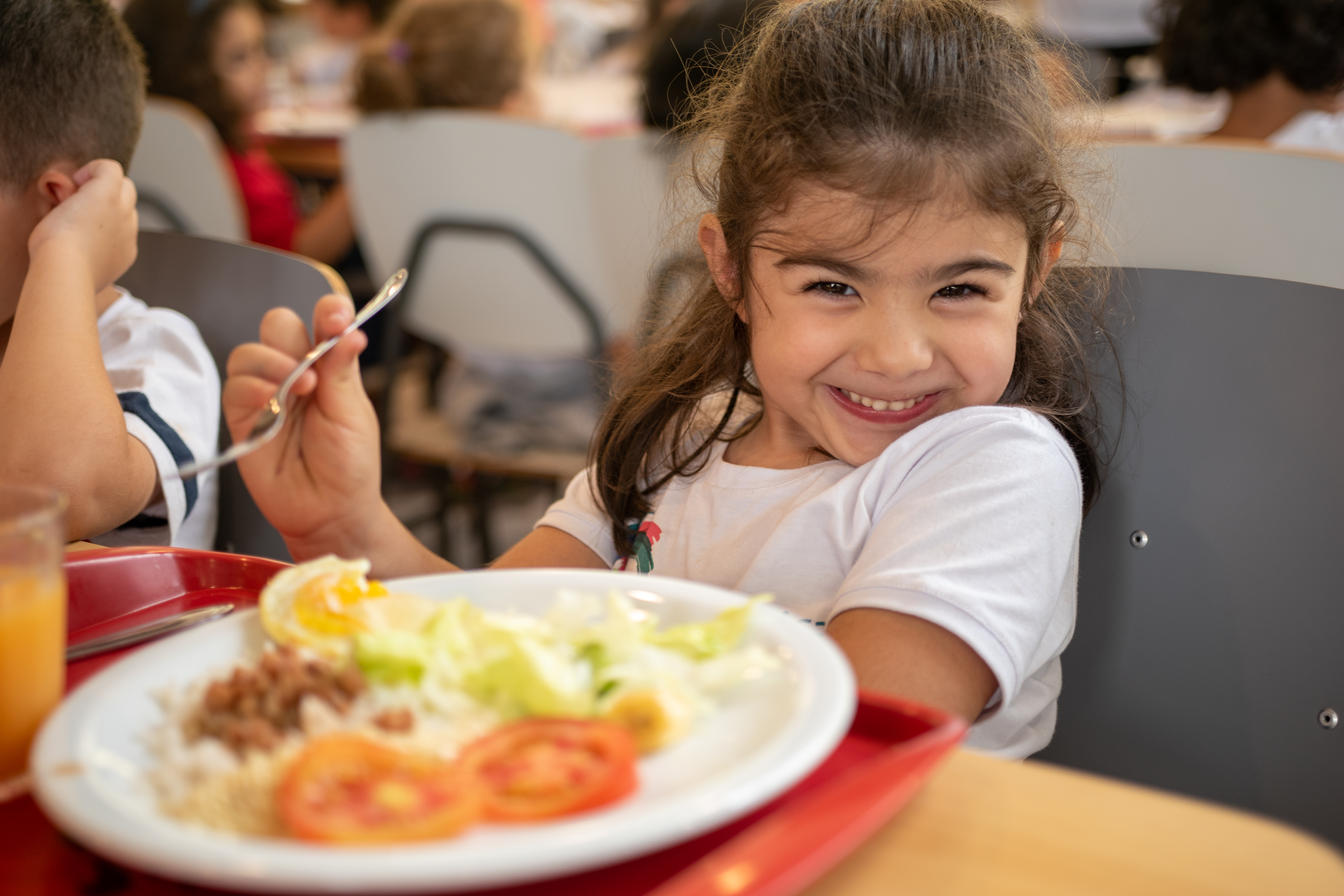 Menina sorrindo com um prato de comida com arroz, feijão e salada
